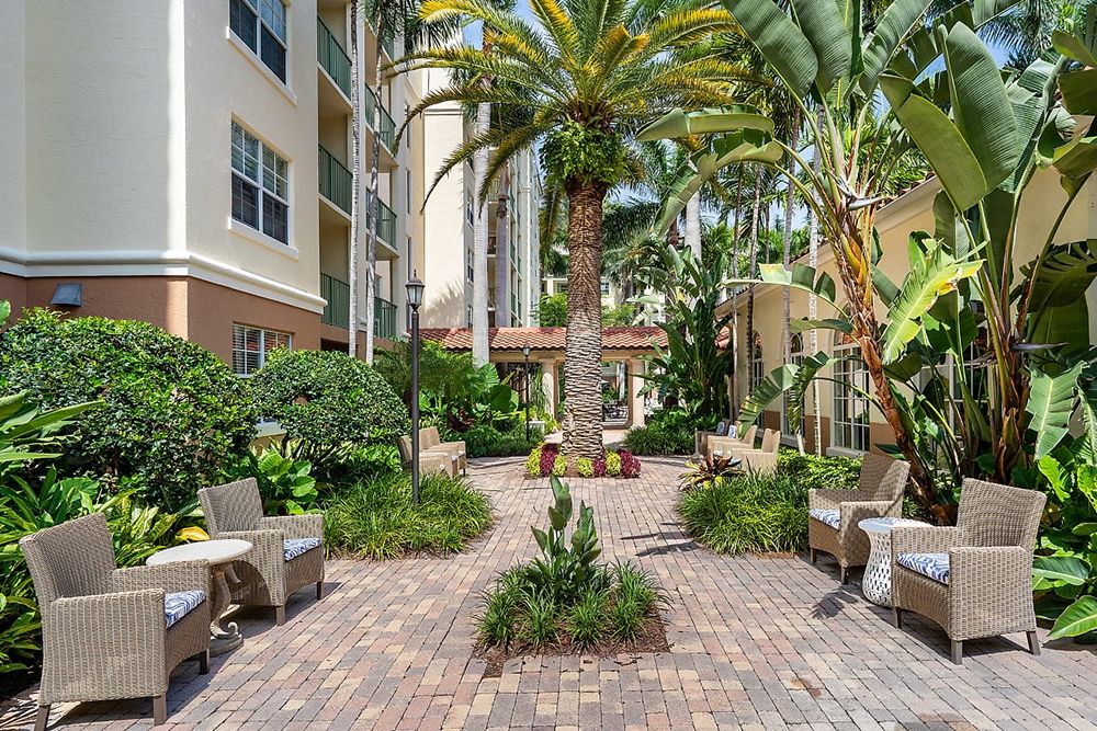 Senior living community, The Carlisle Palm Beach, featuring lush gardens, patio furniture, and villa-style housing.