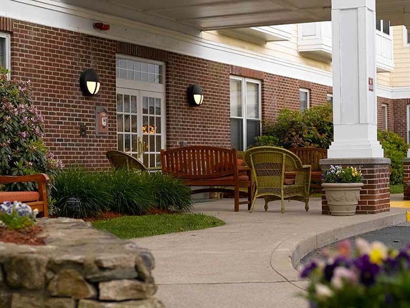 Senior living community, Atria Draper Place, featuring a porch with furniture and lush green yard.