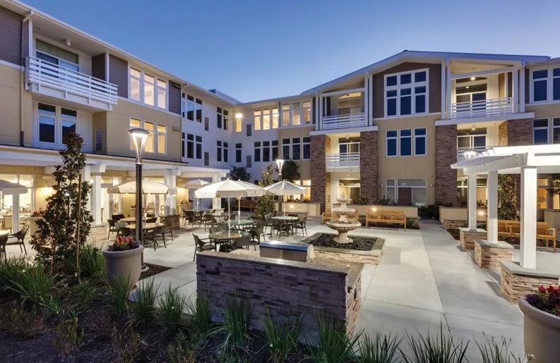 Architectural view of Merrill Gardens senior living condos in urban Huntington Beach, with furniture.