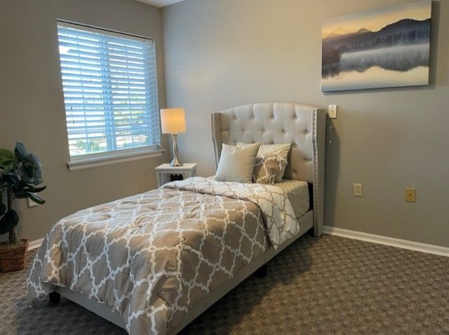 Senior living bedroom at The Village At Primacy Place with bed, lamp, art, and home decor.