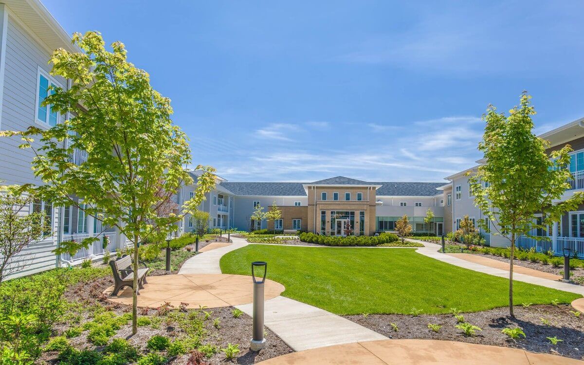 HarborChase of Long Grove senior living community building with outdoor benches, in a lush neighborhood.