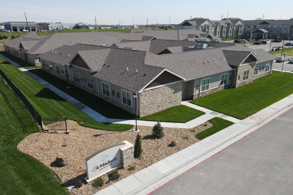 Aerial view of The Wellington Senior Living community featuring houses, a driveway, and a car.