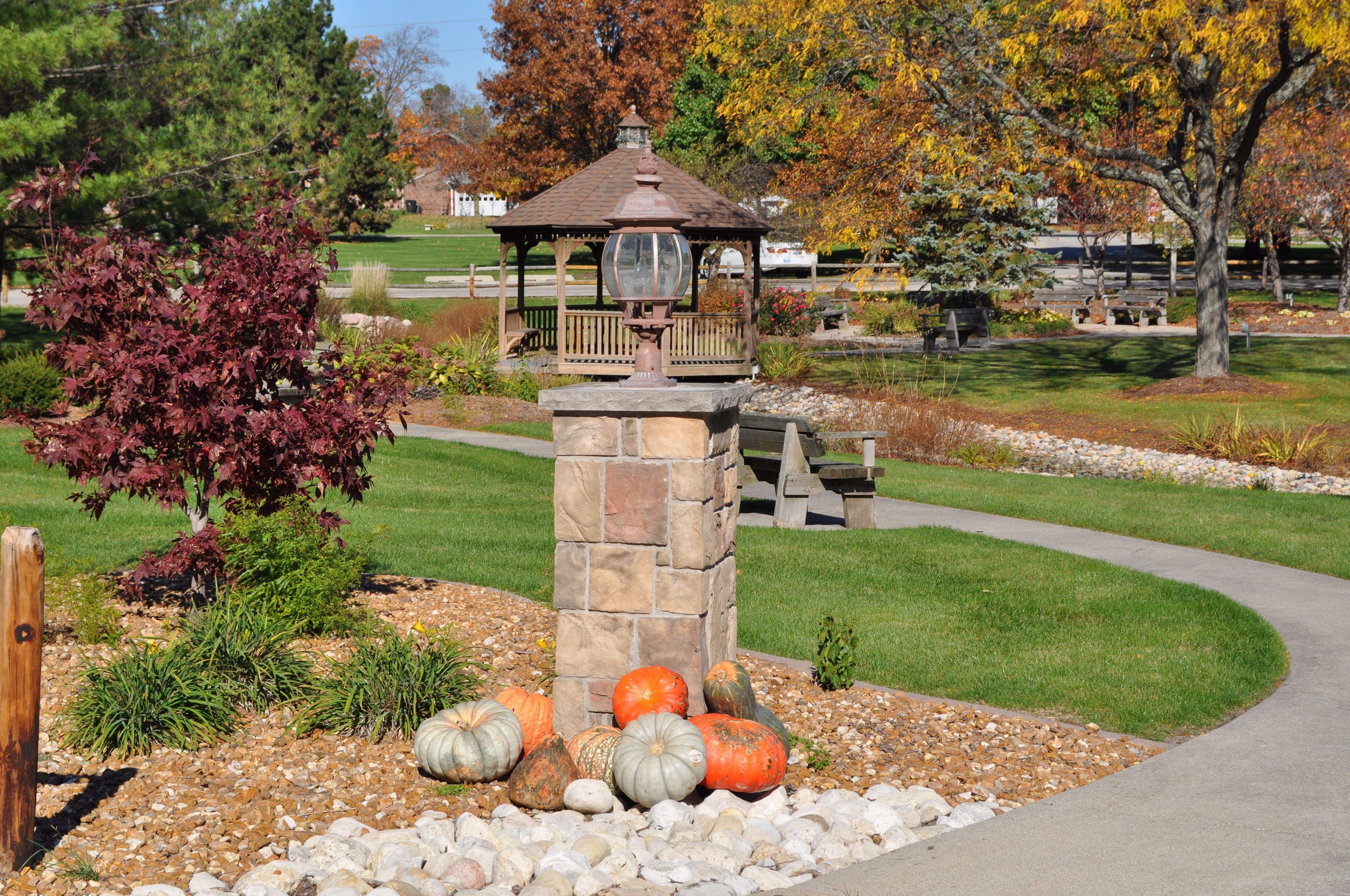 Senior living at Westminster Village with lush greenery, park benches, walking paths, and pumpkin patch.