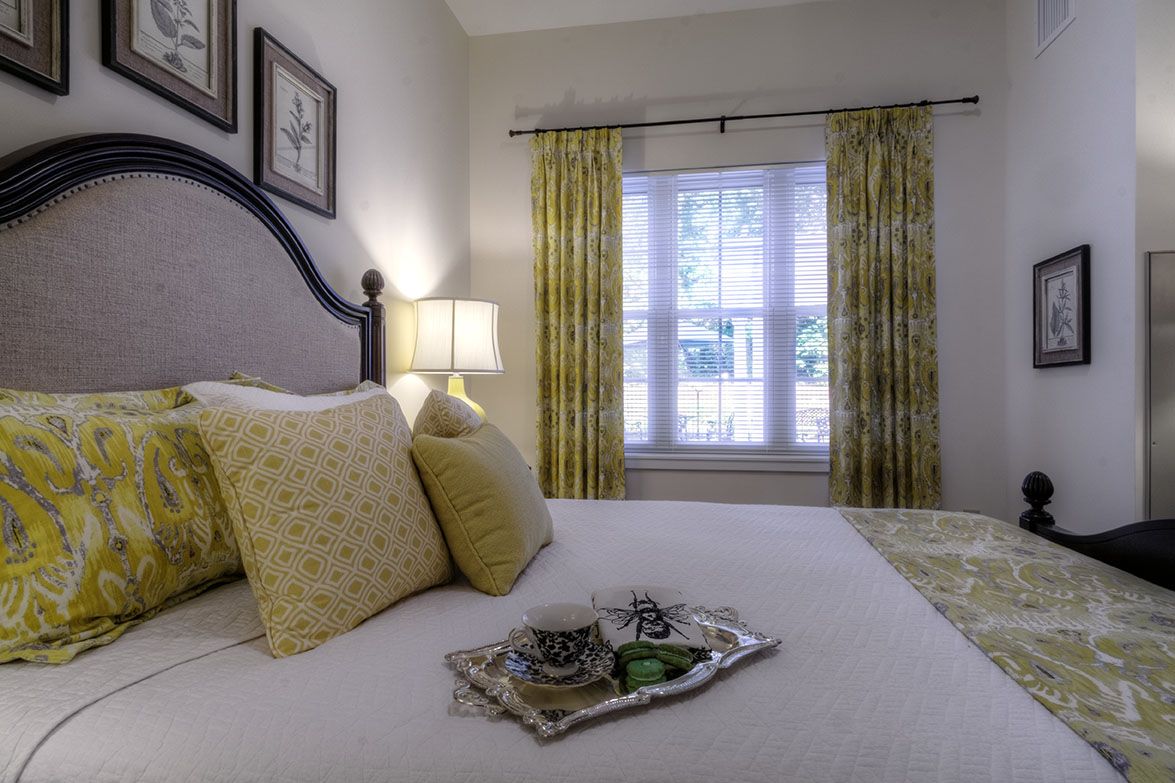 Senior living room at Arbors at Taunton with cozy bed, stylish home decor, and French windows.