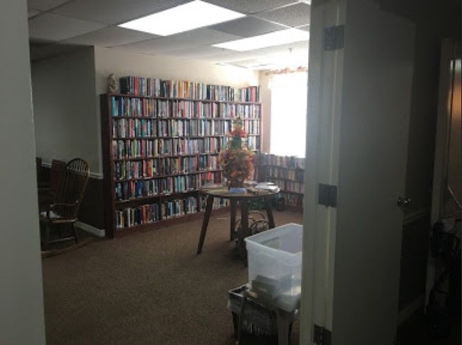 Interior view of Fairway Pines At Sun N Lake senior living community library with bookcases and furniture.