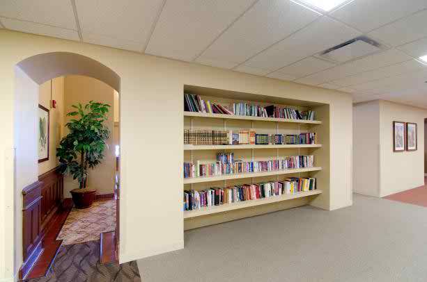 Interior view of Senior Suites Joliet's library with bookcases, furniture, and plants.
