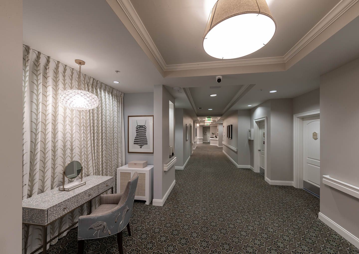 Interior view of The Estate At Hyde Park senior living community featuring a hallway, floor, chandelier, and lamp.
