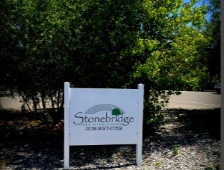 Stonebridge Assisted Living sign amidst lush park with trees, grass and a parked car.