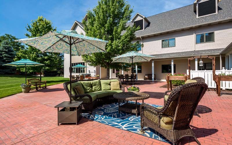 Senior living community, Bickford of West Lansing, featuring outdoor patio, lush yard, and housing architecture.