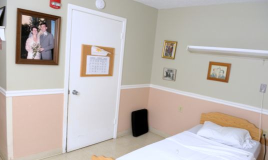 Senior resident in a furnished bedroom at Allenbrooke Nursing and Rehabilitation Center.