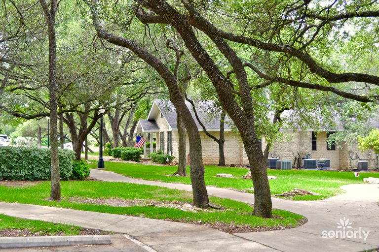 Senior enjoying a stroll in the lush Colonial Gardens of Austin, surrounded by trees, park, and city neighborhood.