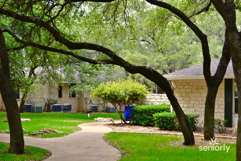 Scenic view of Colonial Gardens senior living in Austin, showcasing lush vegetation, trees, and walkways.
