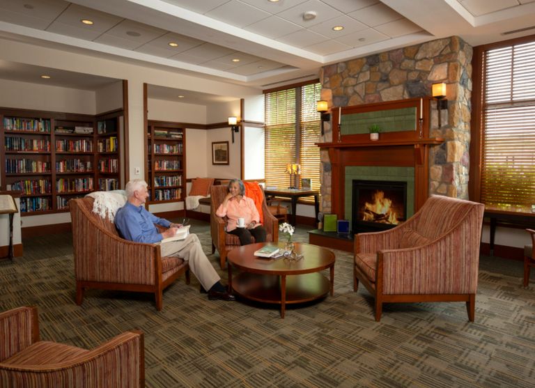 Senior man reading in a cozy living room with fireplace at Waterstone At Wellesley.